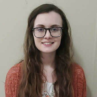 Photo of Kimberly Pinson, long brown hair, glasses, and smiling.