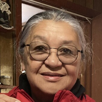 Photo of Marie Bebamikawe, rounded wire-frame glasses, grey hair pulled up or away from face, smiling.