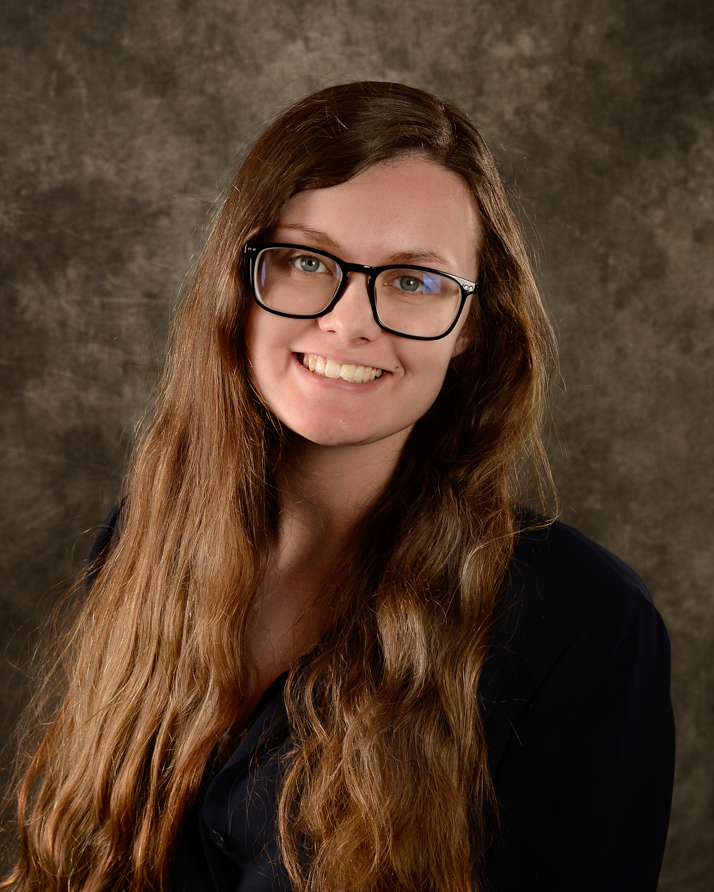 Photo of Kimberly Pinson, long brown hair, glasses, and smiling.