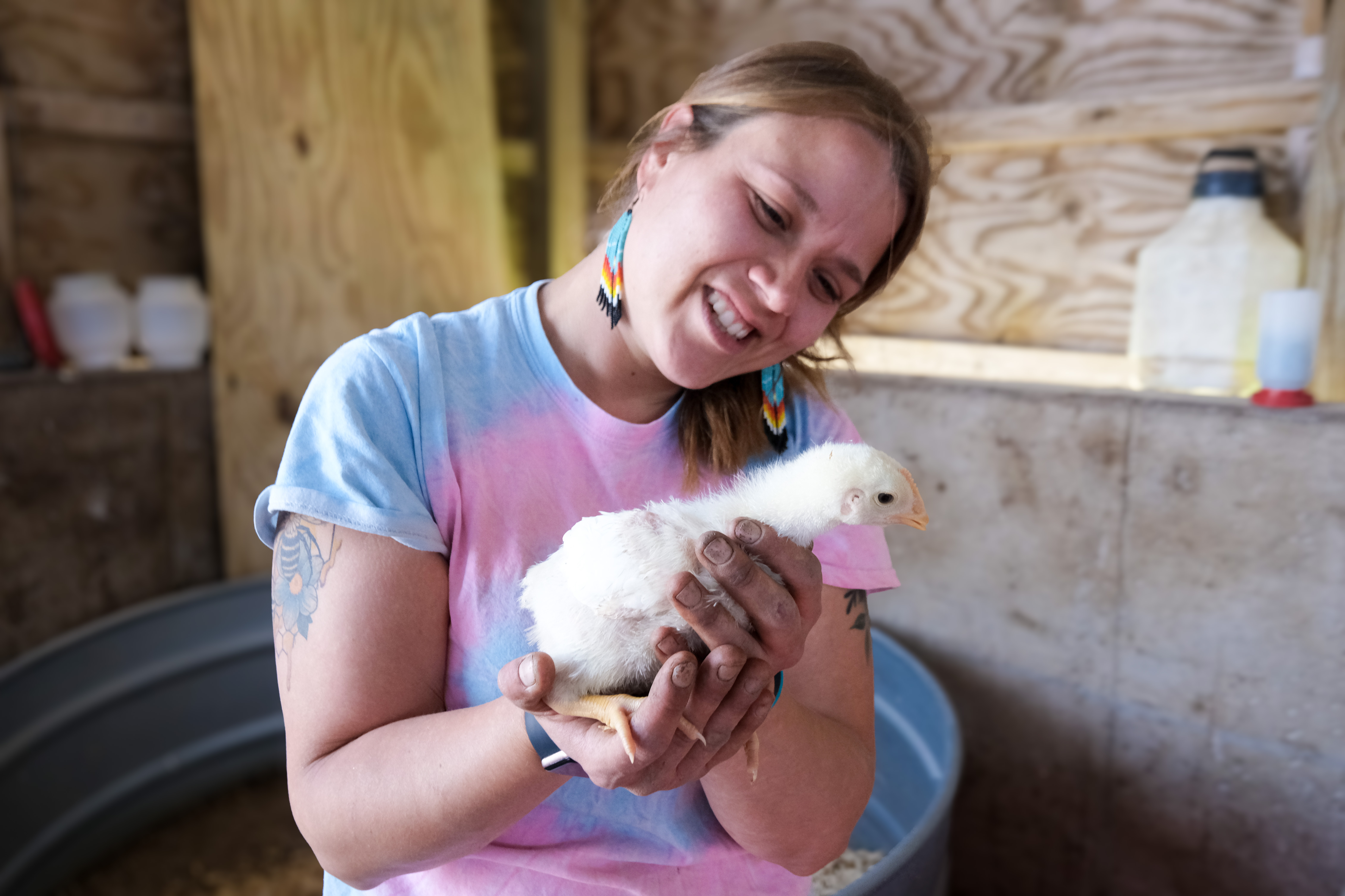 Tori Smith wearing a tye-dye t-shirt, long beaded earrings, holding a white baby chick.
